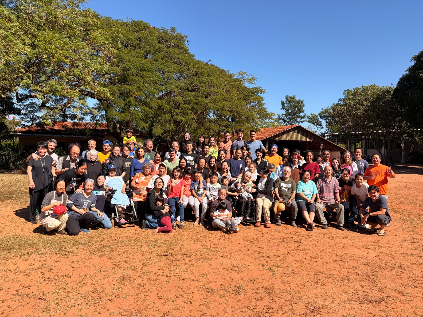 A comunidade reunida sob a grande árvore, em frente às casas: cerca de noventa pessoas de todas as idades, dos mais velhos sentados à frente às crianças no colo.